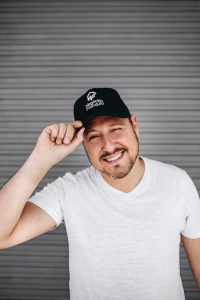 O mineiro que está transformando o repasse de franquias. Fotografia colorida com Rodrigo Campelo segurando o boné da Negócio e Franquia e sorrindo.